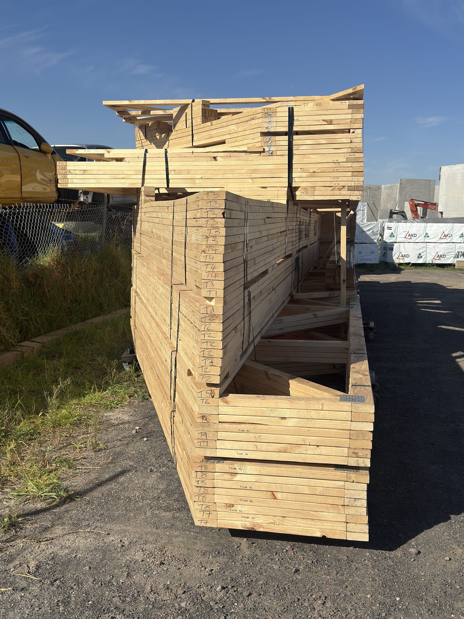 Assembled wall frame with roof truss components visible, marked with hand-written notes, standing at the facility near truck.
